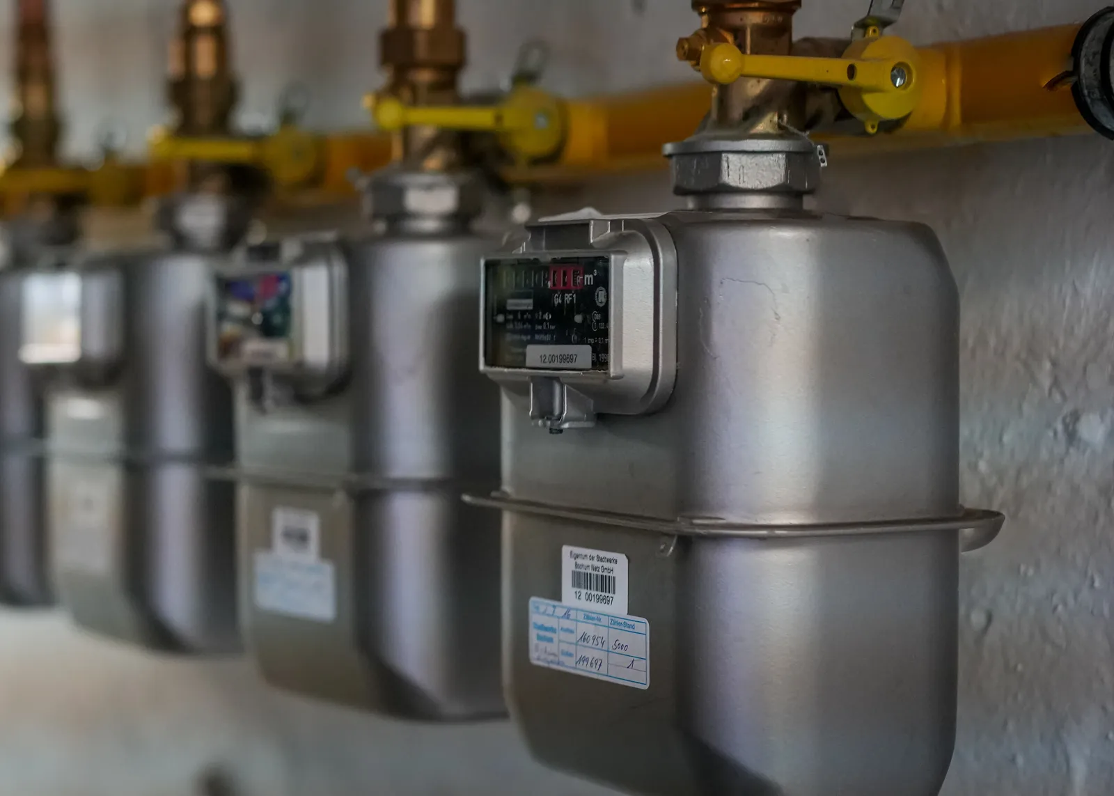 A row of gas meters on a wall, each fed by a brass pipe with a yellow shut-off valve